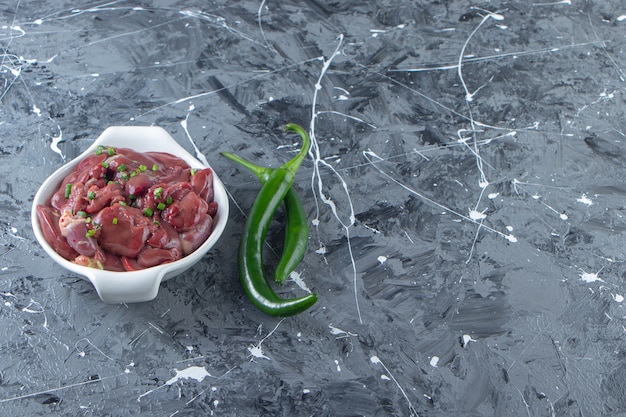 A bowl of chicken offal next to pepper , on the marble background. 