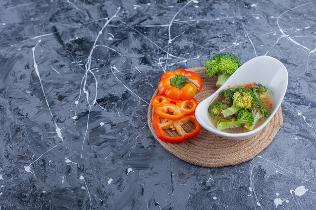 Bowl of chicken soup and vegetables on a trivet, on the blue background. 