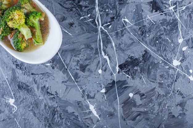 Bowl of chicken soup and vegetables on a trivet, on the blue table.