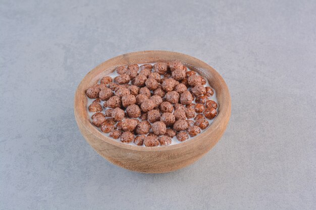 Bowl of chocolate cereal balls with milk on stone table.