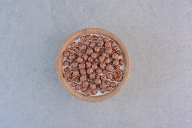 Bowl of chocolate cereal balls with milk on stone.