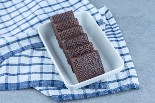 A bowl of chocolate coated on crispy wafer bar on the towel, on the marble table. 