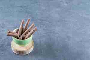 Free photo a bowl of chocolate wafer rolls on a board , on the marble background.