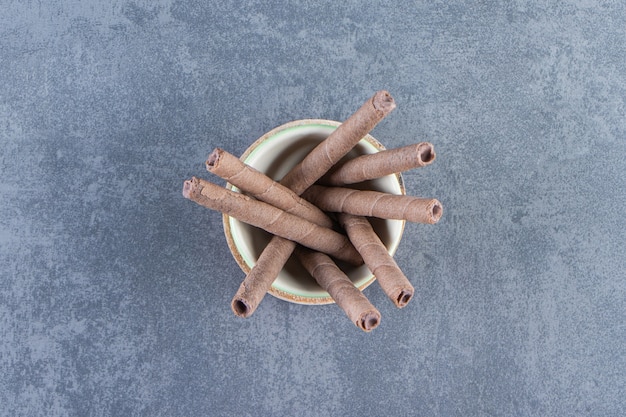 A bowl of chocolate wafer rolls on a board , on the marble background.