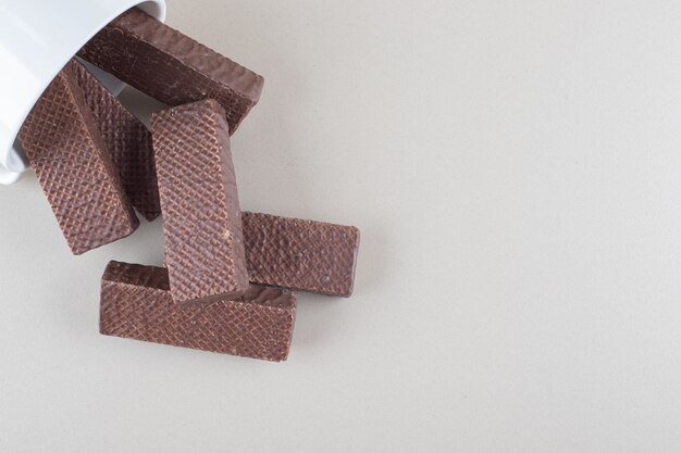 Bowl of chocolate wafers spilled over on marble background.