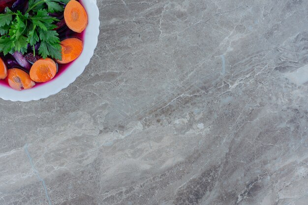 Bowl of chopped beetroots garnished with carrot slices and parsley leaves on marble.