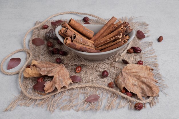 Bowl of cinnamon sticks, leaves and rope on burlap. 