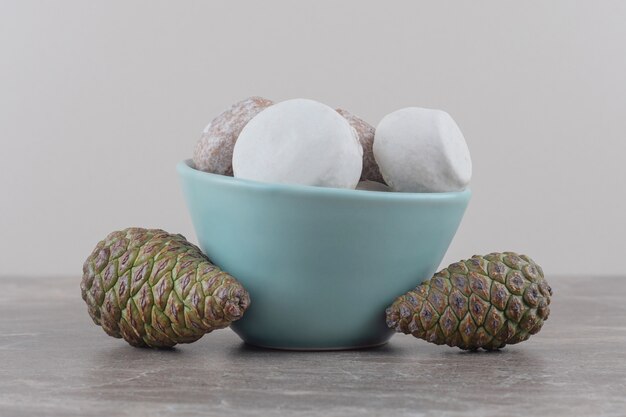 A bowl of cookies next to pine cones on marble 