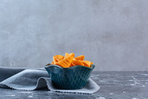 A bowl of crispy potato chips on a piece of fabric , on the marble surface