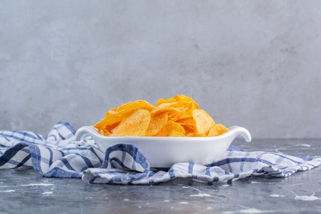 A bowl of delicious potato chips on a tea towel, on the marble surface