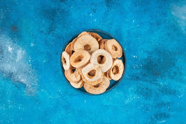 A bowl of dried apple rings on the blue surface