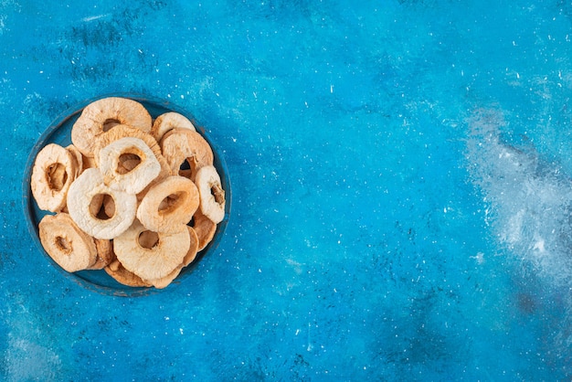 A bowl of dried apple rings on the blue surface