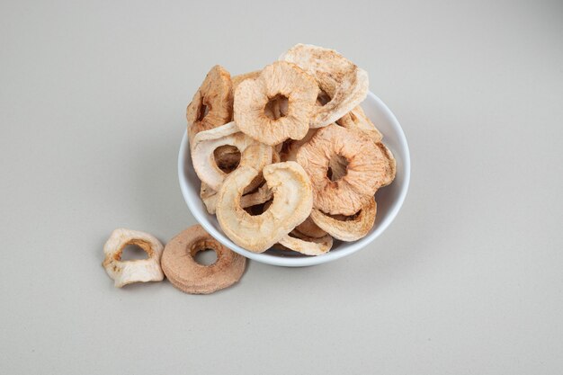 Bowl of dried apple rings on white surface