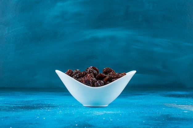 A bowl of dried plums , on the blue table. 