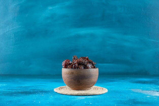 A bowl of dried plums on a trivet on the blue surface