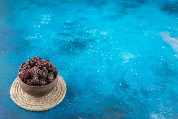 Free photo a bowl of dried plums on a trivet on the blue surface