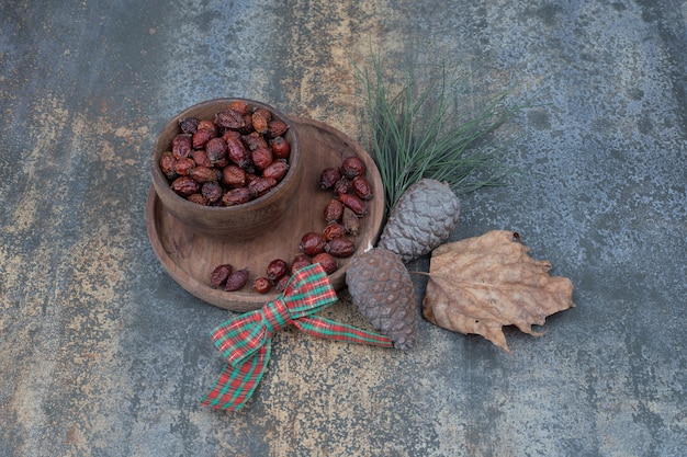 Free photo bowl of dried rose hips, ribbon and pinecones on marble background. high quality photo