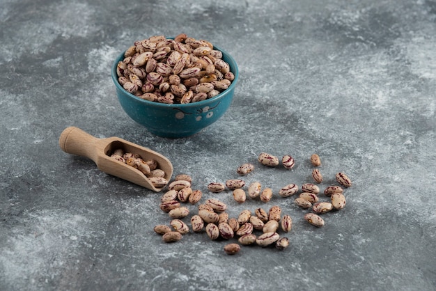 Bowl of dry beans and wooden spoon on marble.