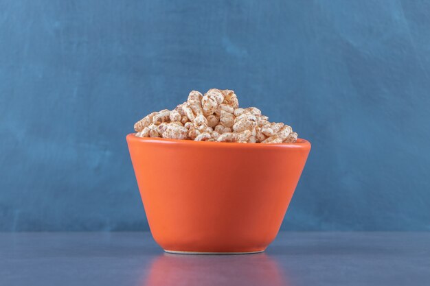 A bowl of dry cornflakes, on the blue table.