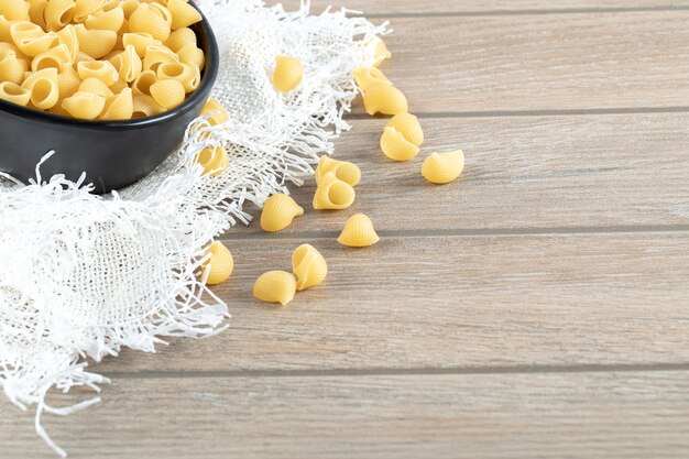 Bowl of dry pasta on wooden table with burlap.