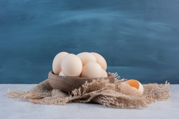 Bowl of eggs next to yolk in a shell on a piece of cloth on marble table.