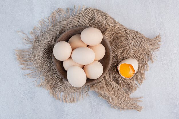 Bowl of eggs next to yolk in a shell on a piece of cloth on marble table.