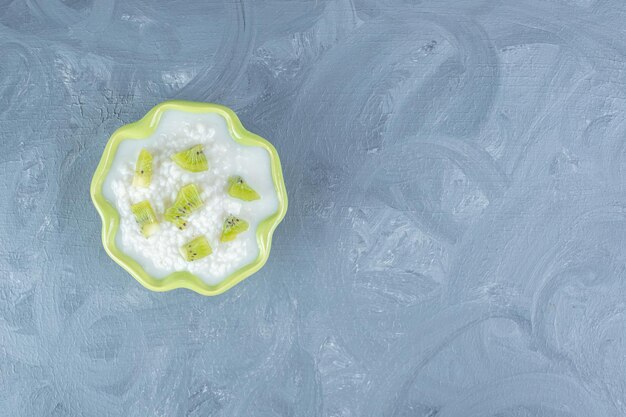 Bowl filled with milky rice and and topped with kiwi bits on marble table.