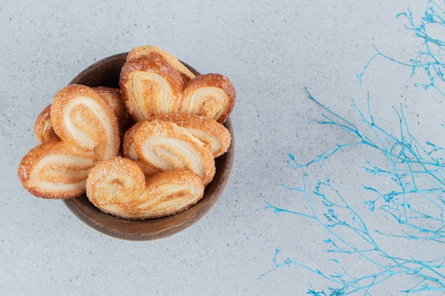 Bowl of flaky cookies and decorative branches on marble background.