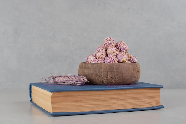 Миска ароматного попкорна и стебель пурпурной пшеницы на книге на мраморном фоне.