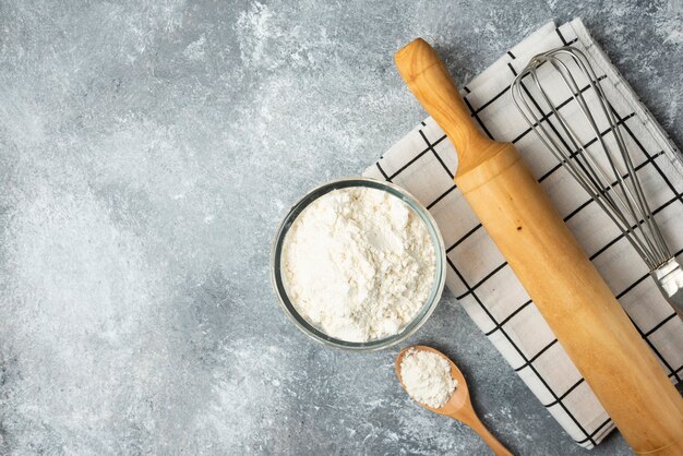 Bowl of flour, eggs and kitchen tools on marble surface.