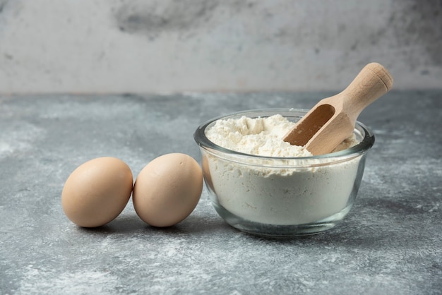 Bowl of flour and eggs on marble table.