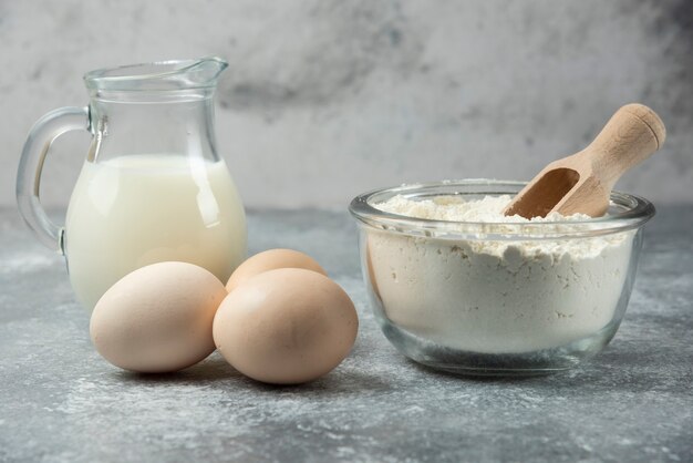 Bowl of flour, eggs and milk on marble table.