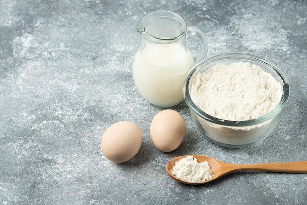 Bowl of flour, eggs and milk on marble.