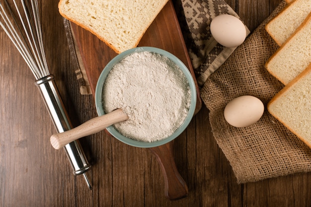 Foto gratuita ciotola di farina con uova e fette di pane