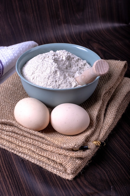 Free photo a bowl of flour with eggs on tablecloth