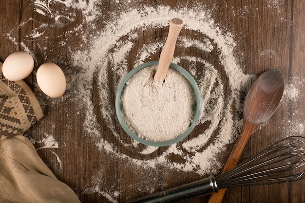 Free photo bowl of flour with eggs and and wooden spoon