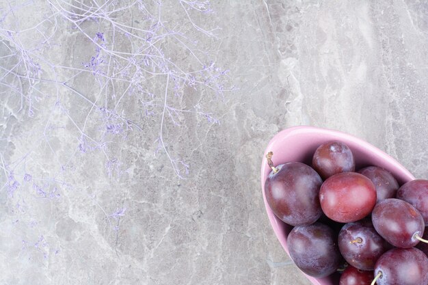 Free photo bowl of fresh plums on stone background.