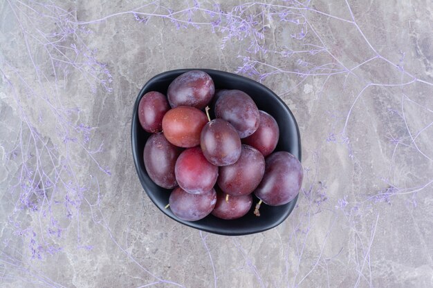 Bowl of fresh plums on stone background. 