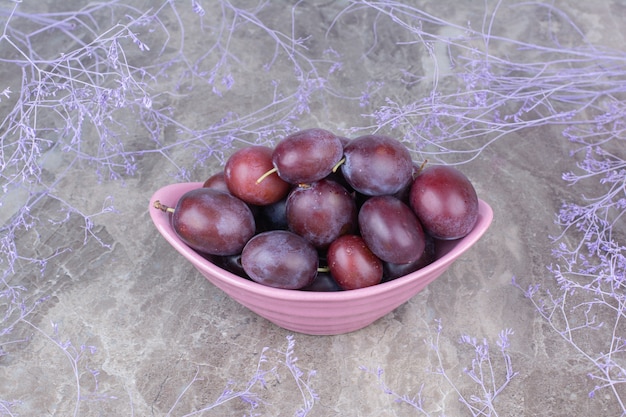 Ciotola di prugne fresche su sfondo di pietra.