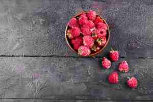 Free photo bowl of fresh red raspberries on dark wooden table.