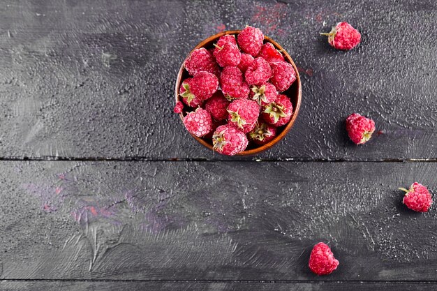 Bowl of fresh red raspberries on dark wooden table. 