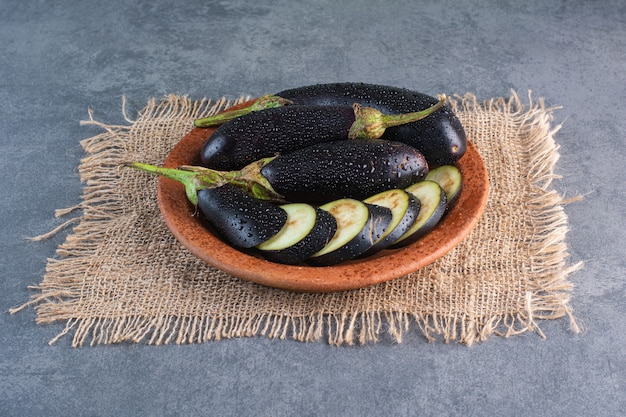 Free photo bowl of fresh ripe eggplants and slices on stone background.