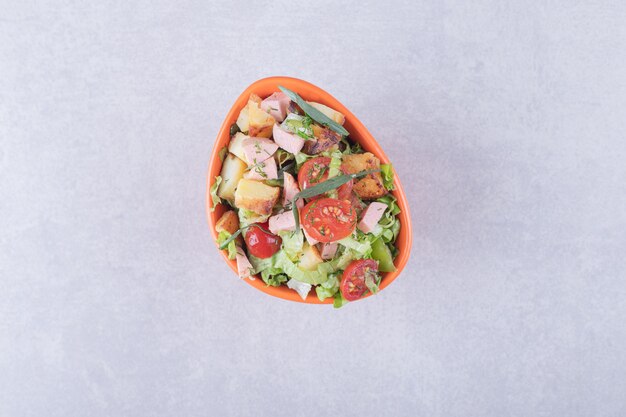 Bowl of fresh salad with sausages on marble background.