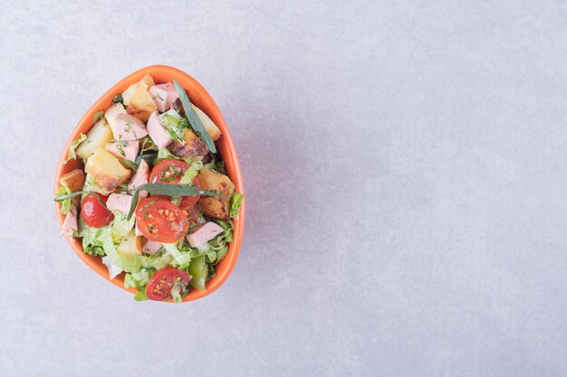 Bowl of fresh salad with sausages on marble background. 