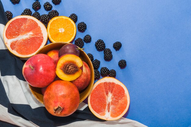 Bowl of fruits; citrus fruit and black berries on blue background