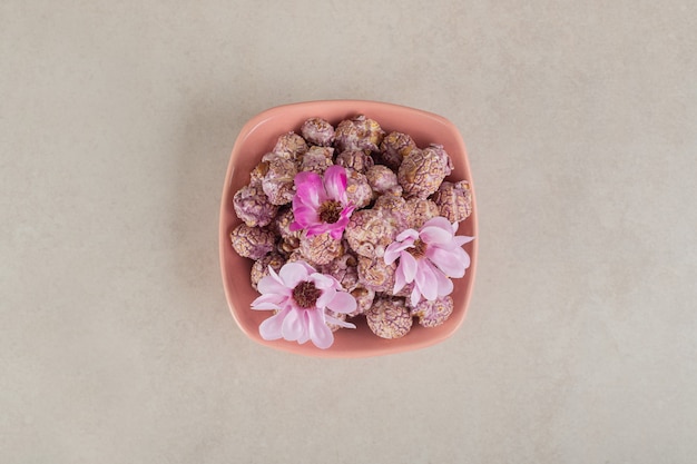 Bowl full of candy coated popcorn topped with flowers on marble.