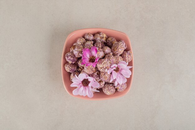 대리석 위에 꽃을 얹은 캔디 코팅 팝콘이 가득한 그릇.