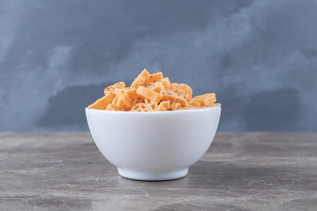 Bowl full of different shaped pasta , on the marble surface.