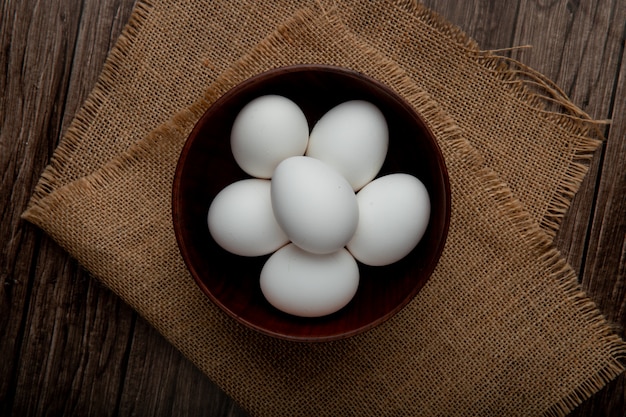 Free photo bowl full of eggs on sackcloth surface and wooden table