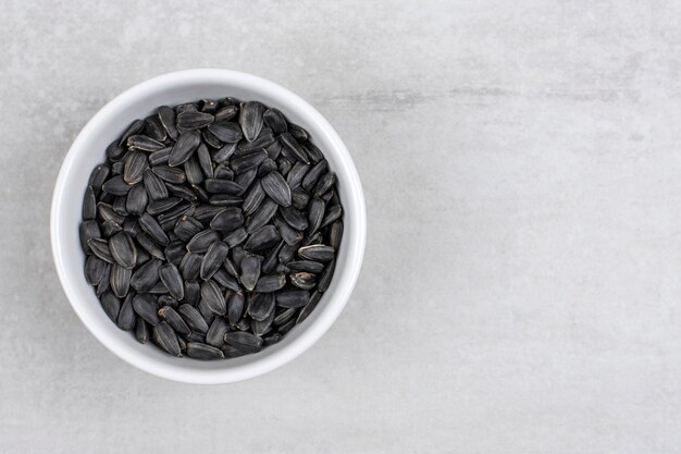 Бесплатное фото Чаша, полная черных семян подсолнечника на камне.